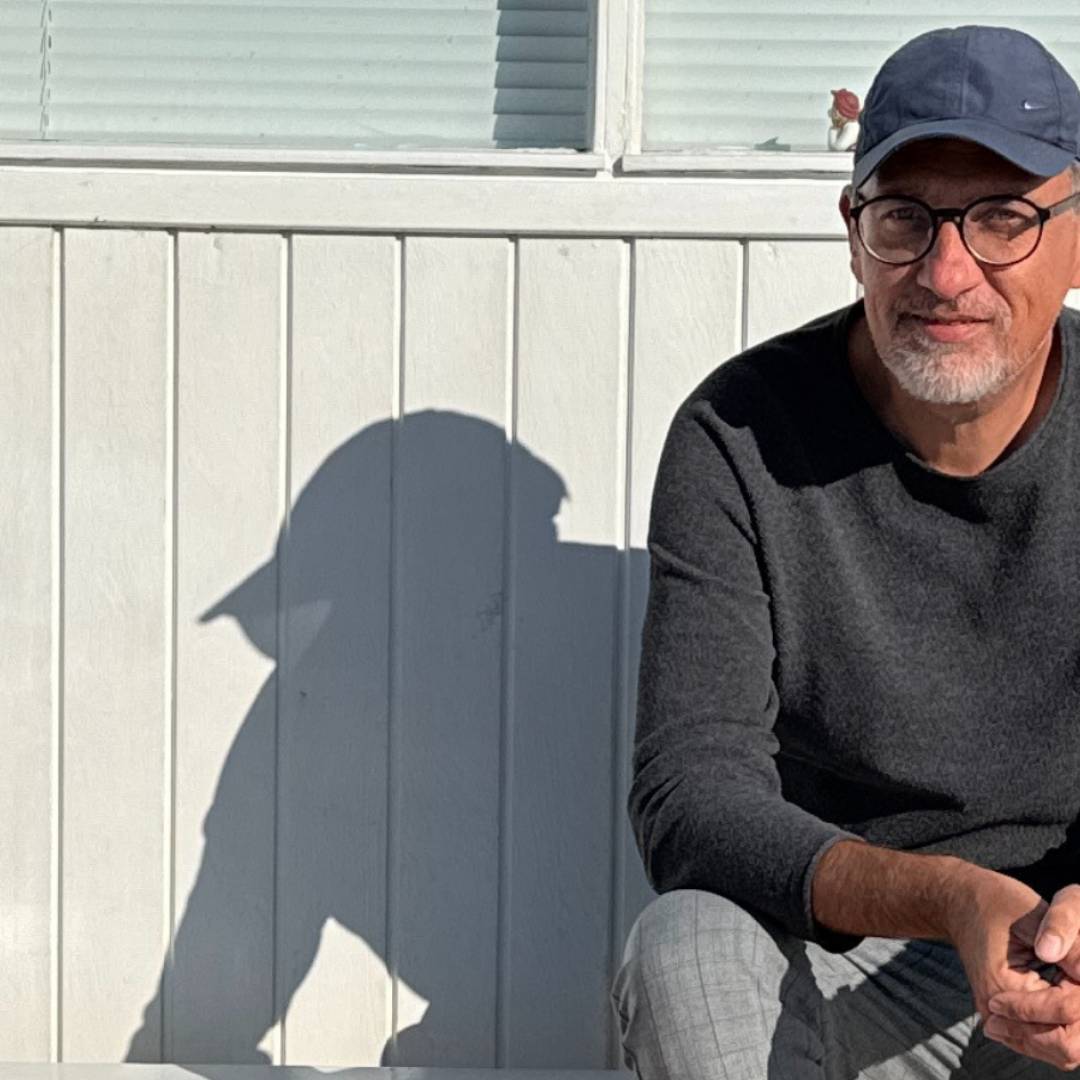 Spirituell leben mit Kay sitzend vor einer weißen Holzwand